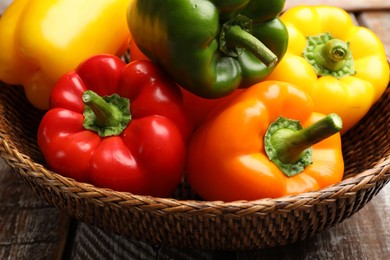 Photo of Fresh colorful bell peppers in wicker basket on table, closeup