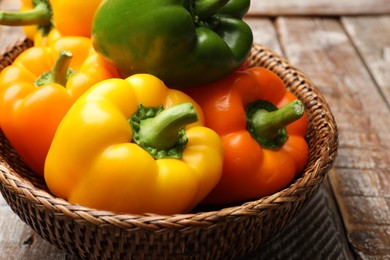 Photo of Fresh colorful bell peppers in wicker basket on wooden table, closeup