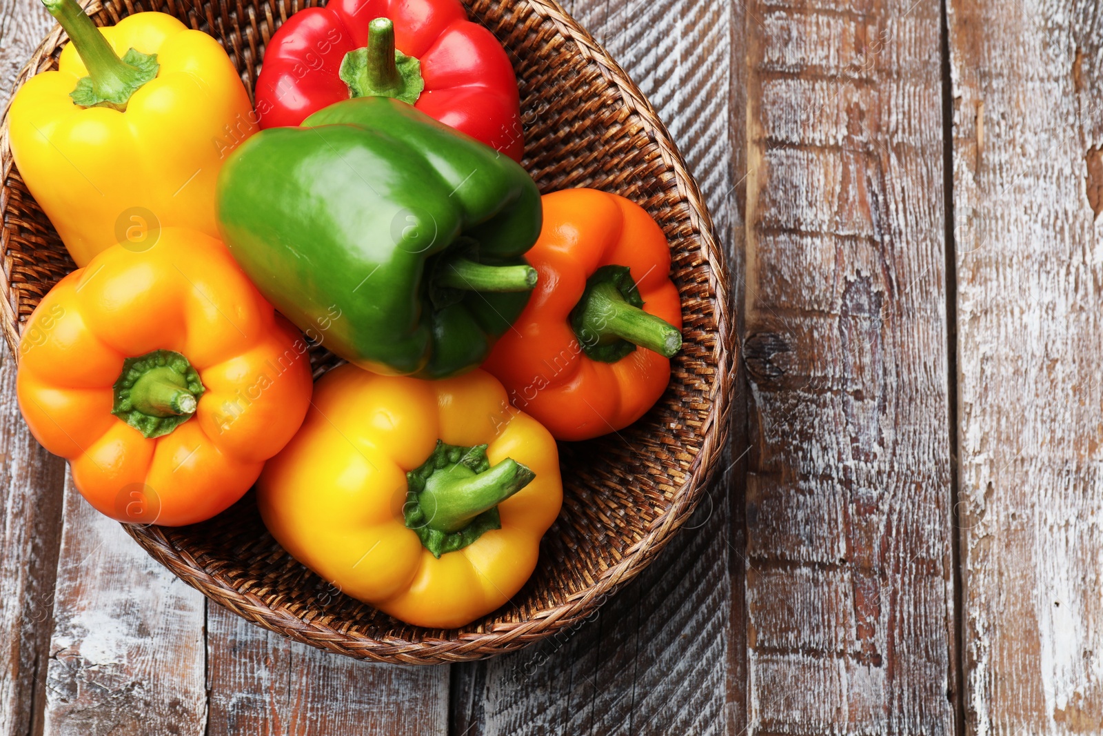 Photo of Fresh colorful bell peppers in wicker basket on wooden table, top view