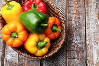 Photo of Fresh colorful bell peppers in wicker basket on wooden table, top view