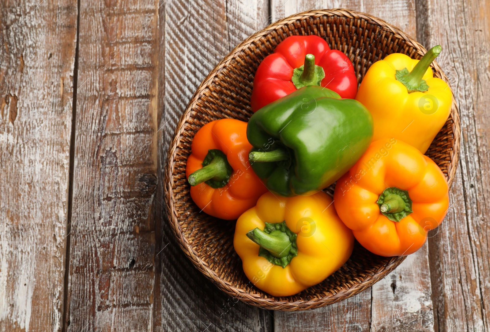 Fresh colorful bell peppers in wicker basket on wooden table, top view Photo of Fresh colorful bell peppers in wicker basket on wooden table, top view