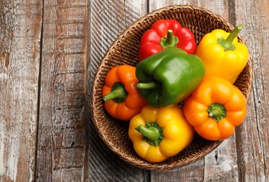 Photo of Fresh colorful bell peppers in wicker basket on wooden table, top view