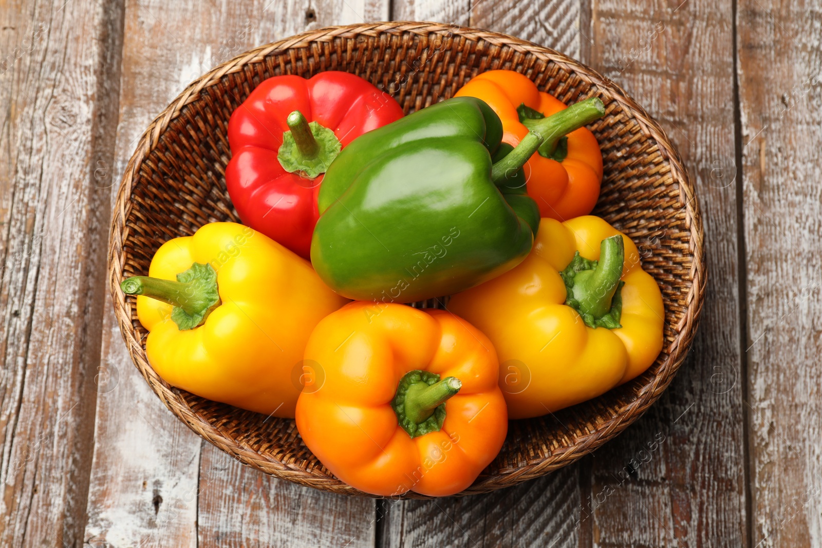 Fresh colorful bell peppers in wicker basket on wooden table, top view Photo of Fresh colorful bell peppers in wicker basket on wooden table, top view