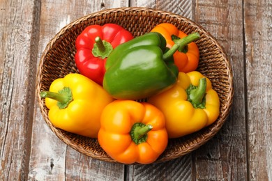 Photo of Fresh colorful bell peppers in wicker basket on wooden table, top view