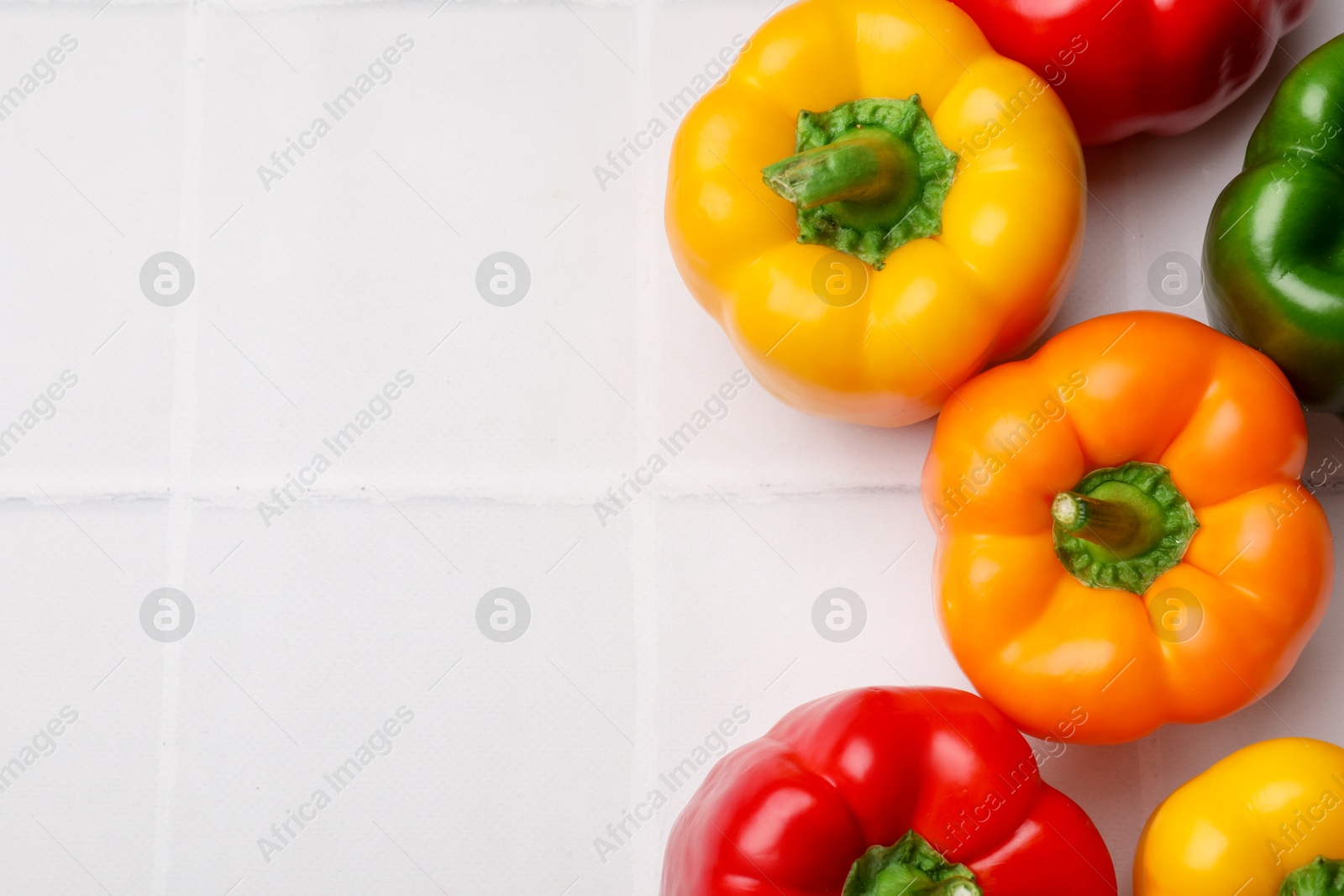 Photo of Fresh colorful bell peppers on white tiled table, flat lay. Space for text