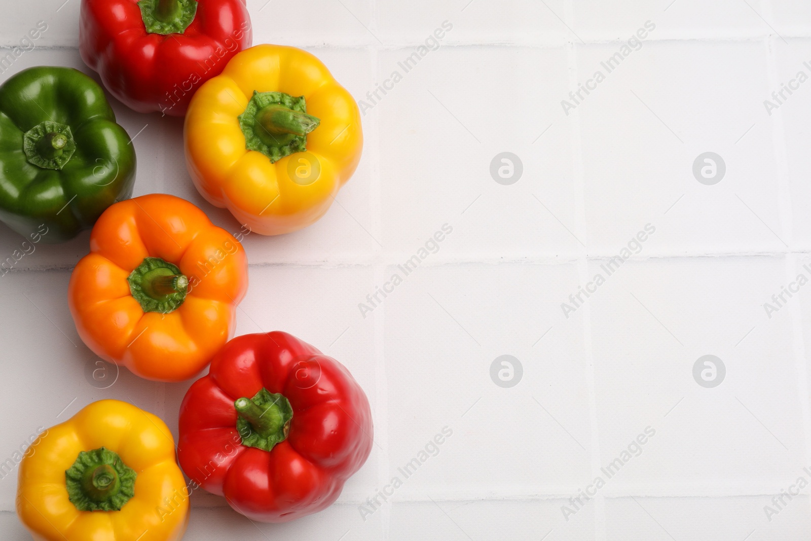 Fresh colorful bell peppers on white tiled table, flat lay. Space for text Photo of Fresh colorful bell peppers on white tiled table, flat lay. Space for text