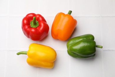 Photo of Fresh colorful bell peppers on white tiled table, flat lay