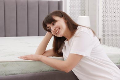 Photo of Woman touching soft mattress on bed indoors