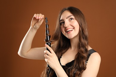 Photo of Beautiful woman curling her hair on brown background