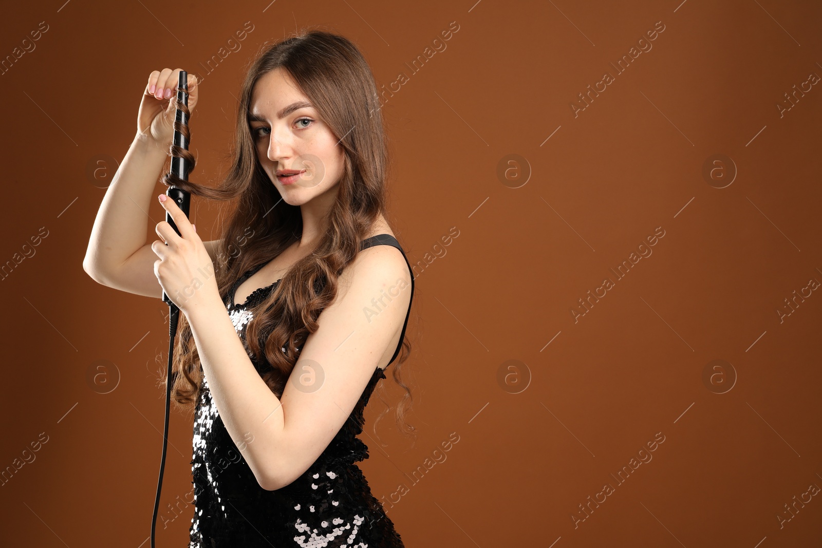 Beautiful woman curling her hair on brown background. Space for text Photo of Beautiful woman curling her hair on brown background. Space for text