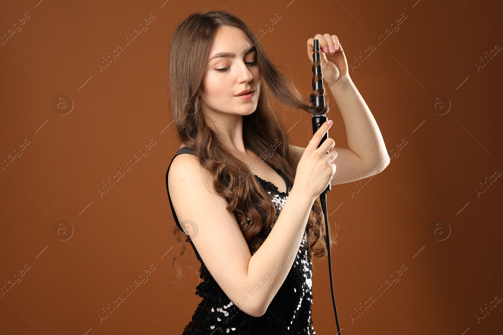 Beautiful woman curling her hair on brown background Photo of Beautiful woman curling her hair on brown background