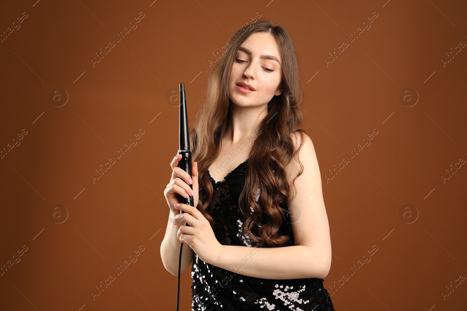 Woman with beautiful hairstyle and curling iron on brown background Photo of Woman with beautiful hairstyle and curling iron on brown background