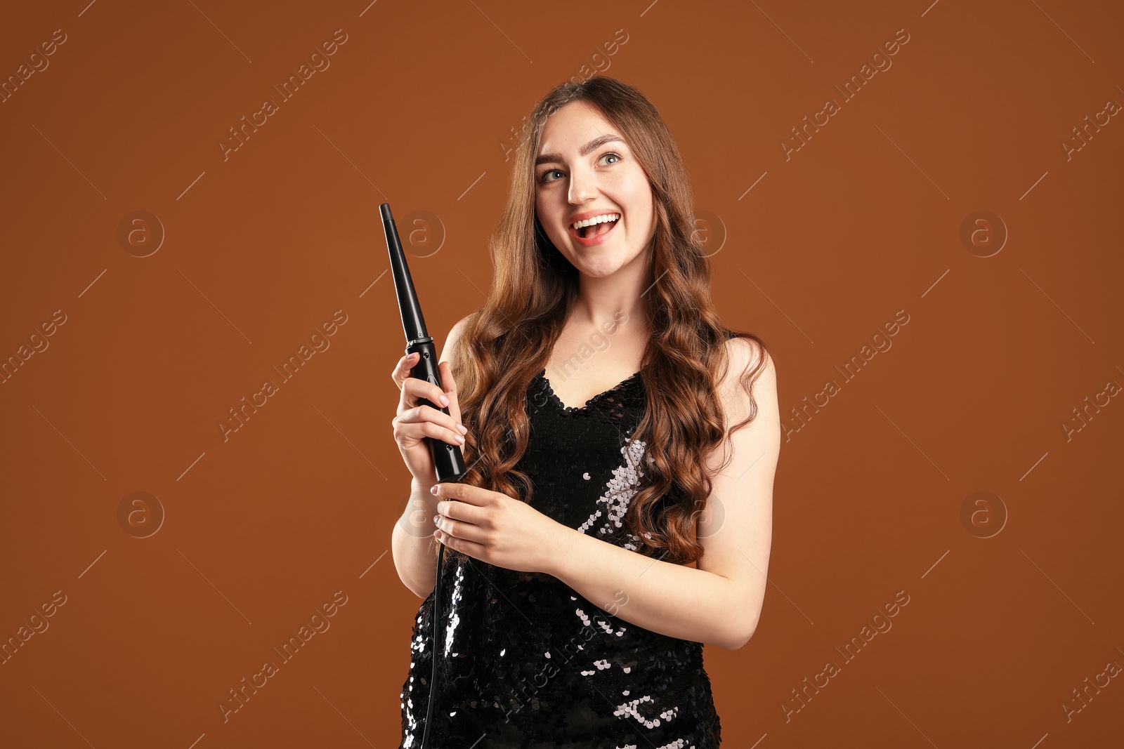 Woman with beautiful hairstyle and curling iron on brown background Photo of Woman with beautiful hairstyle and curling iron on brown background