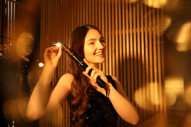 Photo of Woman curling her beautiful hair in dressing room