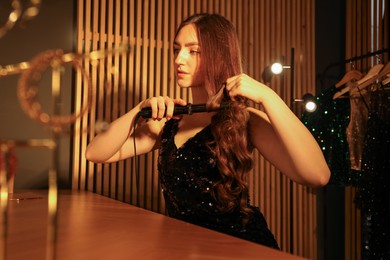 Photo of Woman curling her beautiful hair in dressing room