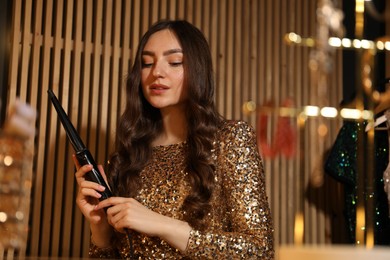 Photo of Woman curling her beautiful hair in dressing room