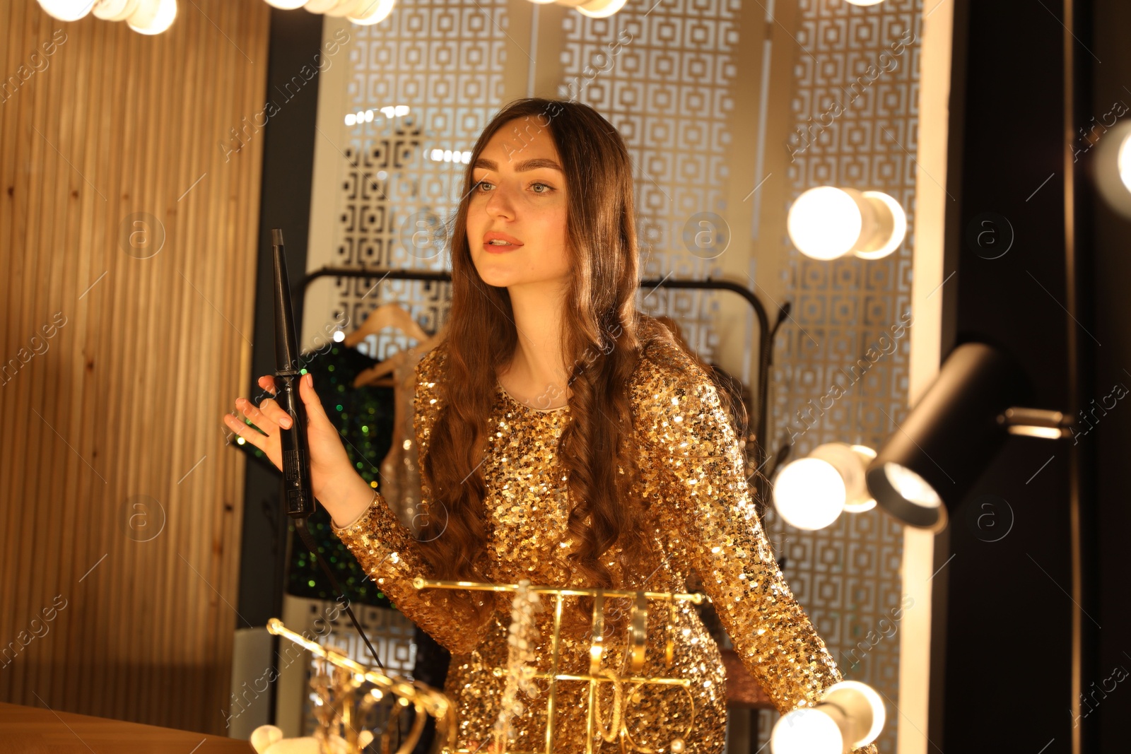 Woman curling her beautiful hair near mirror indoors Photo of Woman curling her beautiful hair near mirror indoors