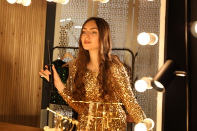 Photo of Woman curling her beautiful hair near mirror indoors