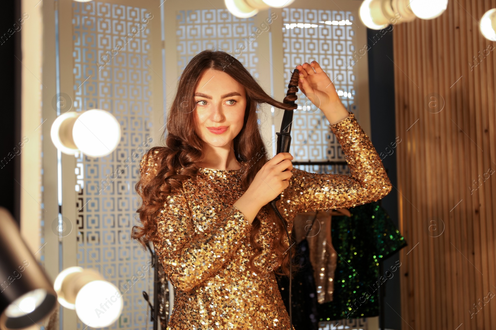 Woman curling her beautiful hair near mirror indoors Photo of Woman curling her beautiful hair near mirror indoors