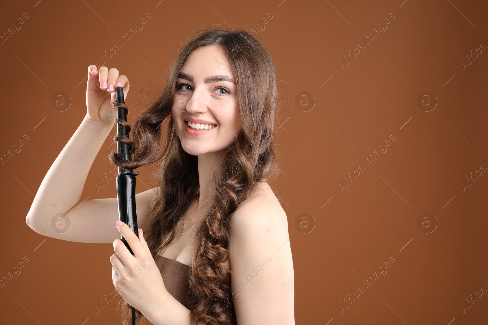 Woman curling her beautiful hair on brown background. Space for text Photo of Woman curling her beautiful hair on brown background. Space for text