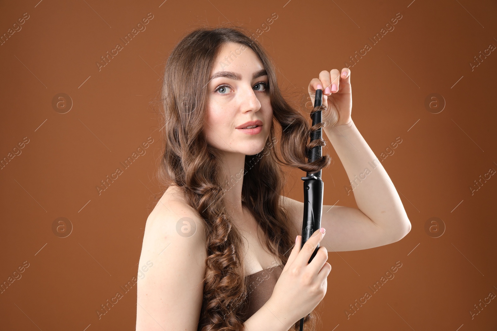 Woman curling her beautiful hair on brown background Photo of Woman curling her beautiful hair on brown background