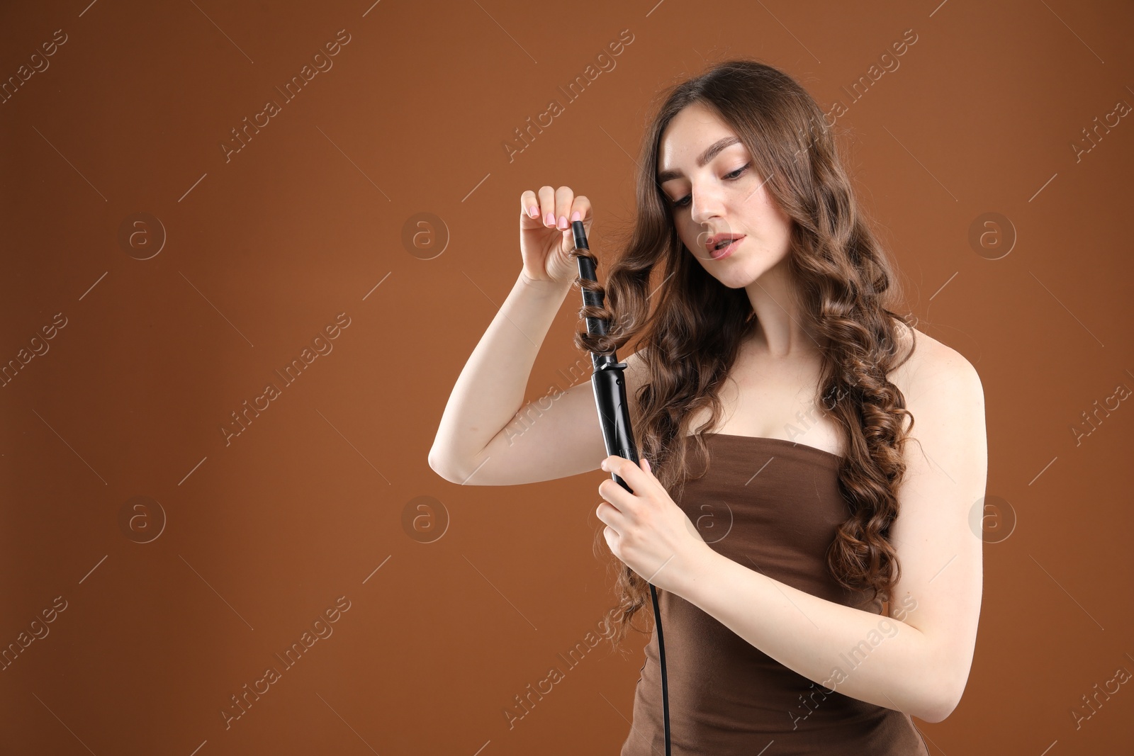 Woman curling her beautiful hair on brown background. Space for text Photo of Woman curling her beautiful hair on brown background. Space for text