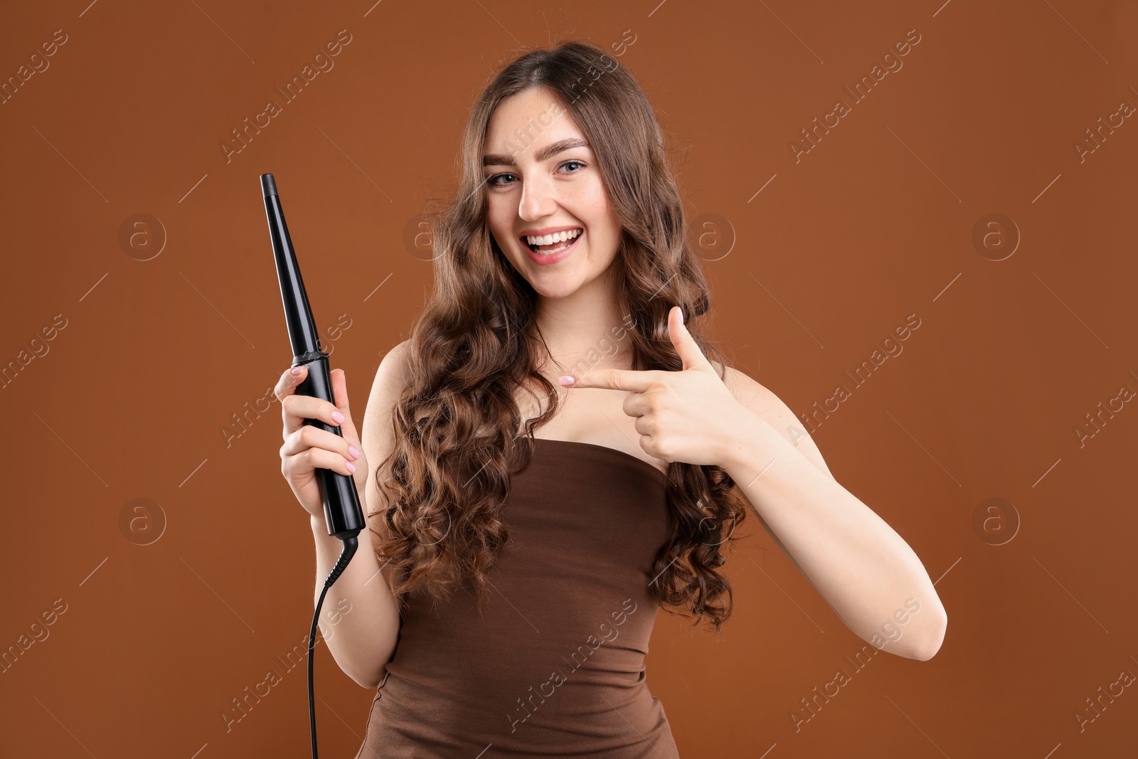 Woman curling her beautiful hair on brown background Photo of Woman curling her beautiful hair on brown background
