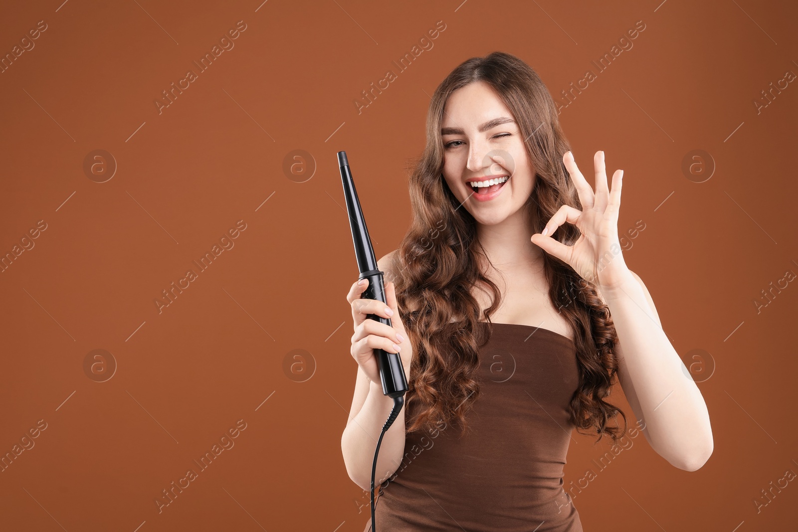 Woman curling her beautiful hair on brown background. Space for text Photo of Woman curling her beautiful hair on brown background. Space for text