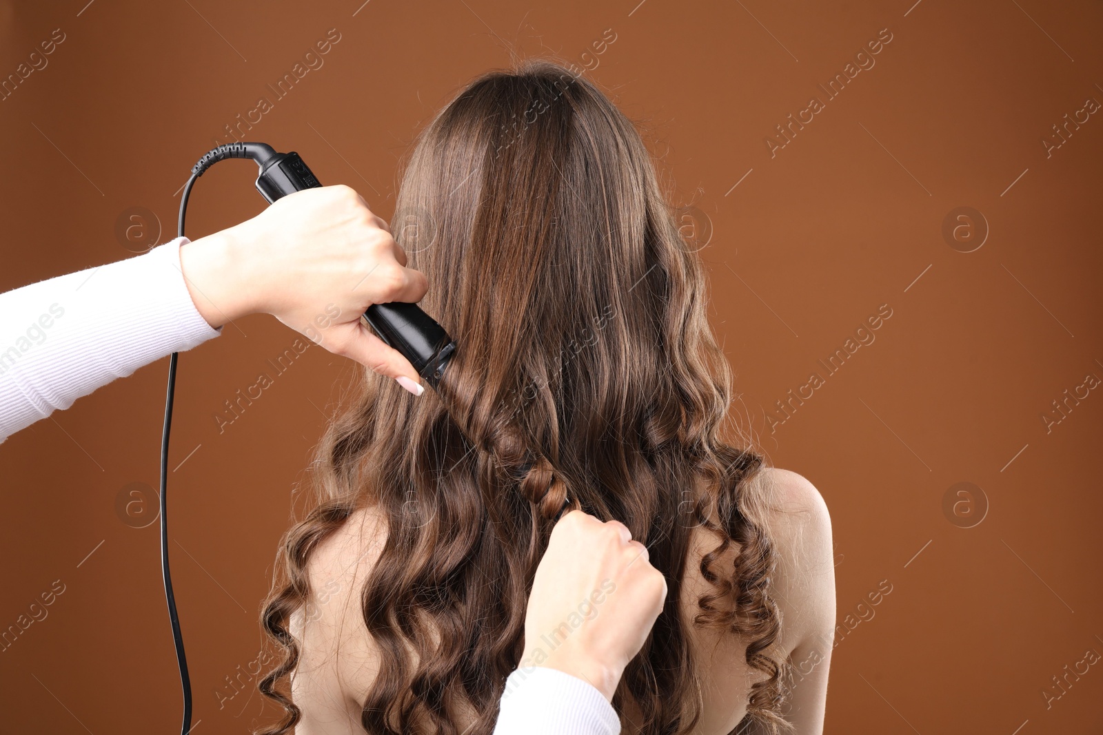 Hairdresser curling woman's hair on brown background, back view Photo of Hairdresser curling woman's hair on brown background, back view