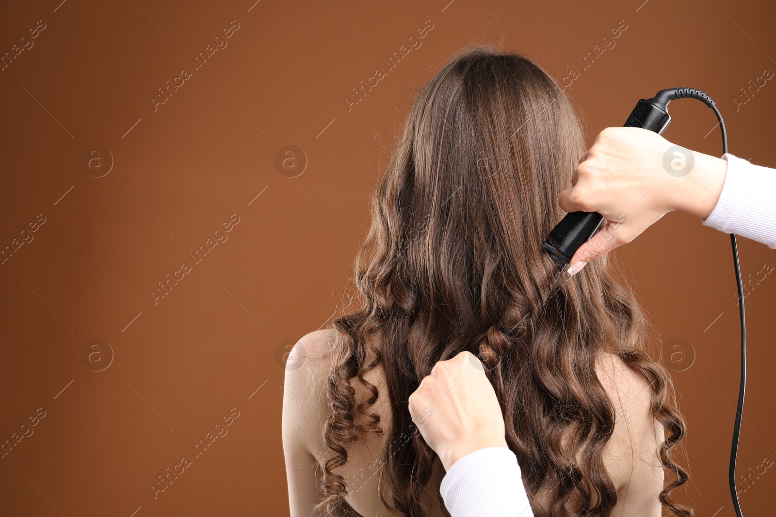 Hairdresser curling woman's hair on brown background, back view. Space for text Photo of Hairdresser curling woman's hair on brown background, back view. Space for text