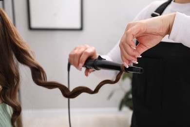 Photo of Hairdresser curling woman's hair in salon, closeup
