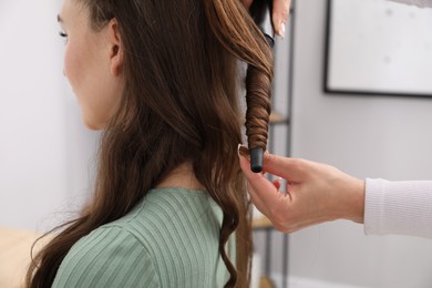 Photo of Hairdresser curling woman's hair in salon, closeup