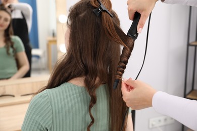 Photo of Hairdresser curling woman's hair in salon, closeup