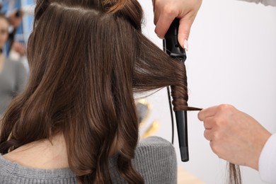 Photo of Hairdresser curling woman's hair in salon, closeup