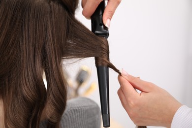 Photo of Hairdresser curling woman's hair in salon, closeup. Space for text