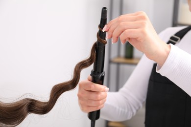 Photo of Hairdresser curling woman's hair in salon, closeup. Space for text