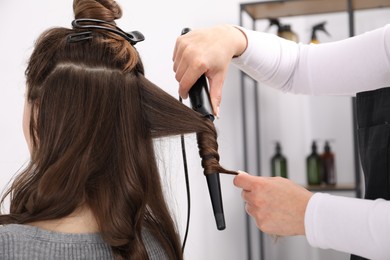 Photo of Hairdresser curling woman's hair in salon, closeup