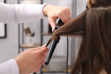 Photo of Hairdresser curling woman's hair in salon, closeup