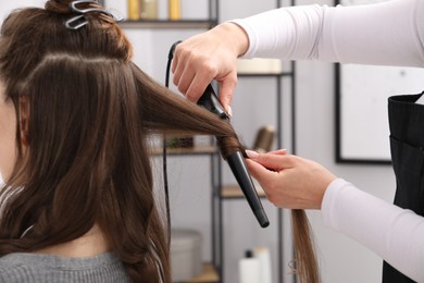 Photo of Hairdresser curling woman's hair in salon, closeup