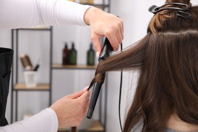 Photo of Hairdresser curling woman's hair in salon, closeup