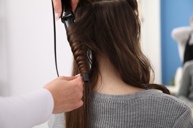 Photo of Hairdresser curling woman's hair in salon, closeup