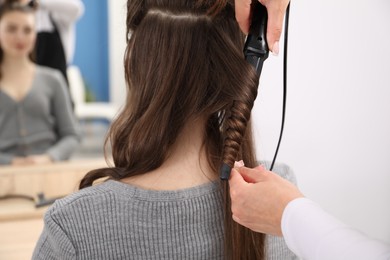 Photo of Hairdresser curling woman's hair in salon, closeup