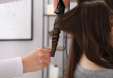 Photo of Hairdresser curling woman's hair in salon, closeup. Space for text