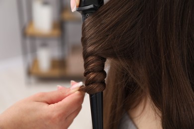 Photo of Hairdresser curling woman's hair in salon, closeup
