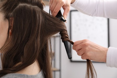 Photo of Hairdresser curling woman's hair in salon, closeup