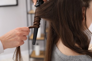 Photo of Hairdresser curling woman's hair in salon, closeup
