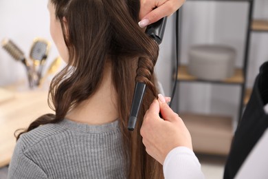 Photo of Hairdresser curling woman's hair in salon, closeup