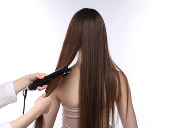 Photo of Hairdresser straightening woman's hair on white background, back view