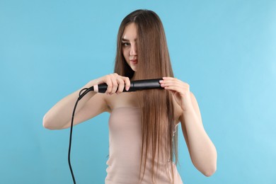 Photo of Woman straightening her beautiful hair on light blue background