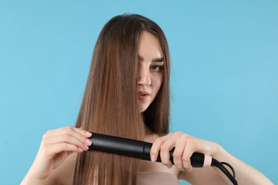 Photo of Woman straightening her beautiful hair on light blue background